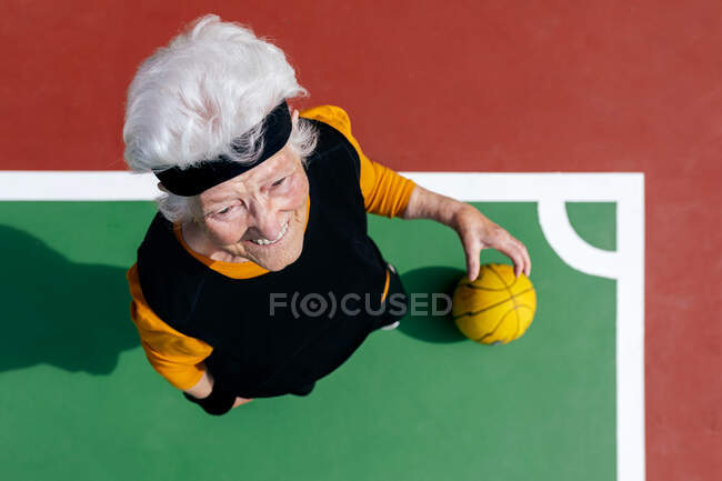 Вид зверху на зрілу жінку з сірим волоссям, що стоїть на спортивному майданчику з м'ячем під час гри в баскетбол — стокове фото