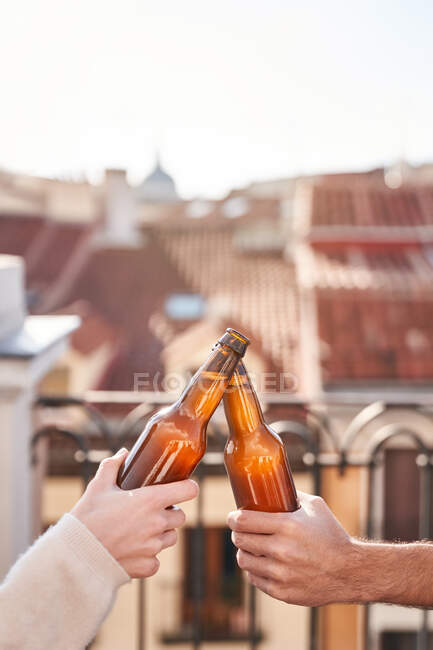 Неузнаваемые молодые друзья звенят бутылками пива, расслабляясь на террасе вместе — стоковое фото