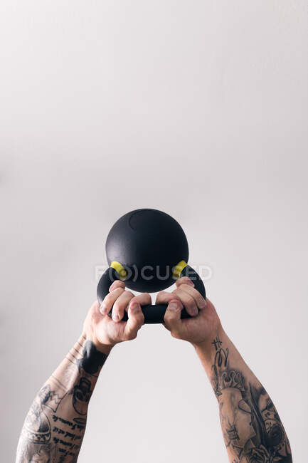 Concentre-se homem forte fisiculturista com tatuagens levantando kettlebell pesado treinamento branco no ginásio contra a parede leve — Fotografia de Stock