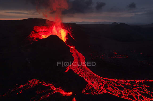 Сверху извергающийся вулкан и горячая красная магма, текущая по темной горной поверхности ночью в высокогорье Исландии в темноте — стоковое фото