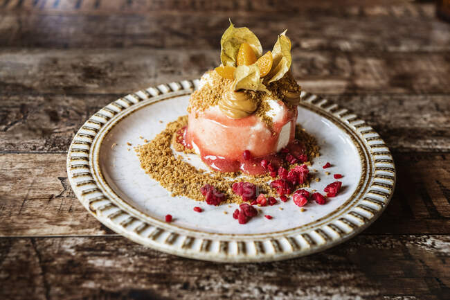 Leckeres Dessert mit Sahne und reifen Physalis-Beeren bestreut Kekskrümel auf weißem Teller auf Holztisch im Restaurant serviert — Stockfoto