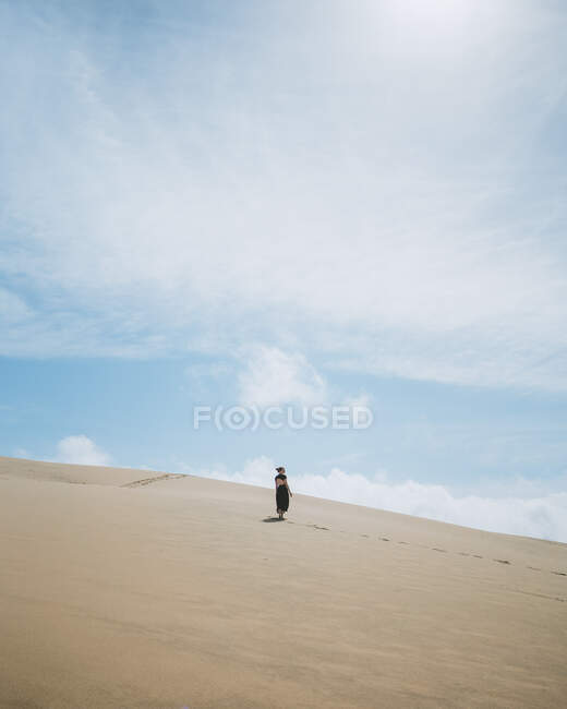 Full body back view of barefoot female in dress strolling on sandy dune in desert — Stock Photo