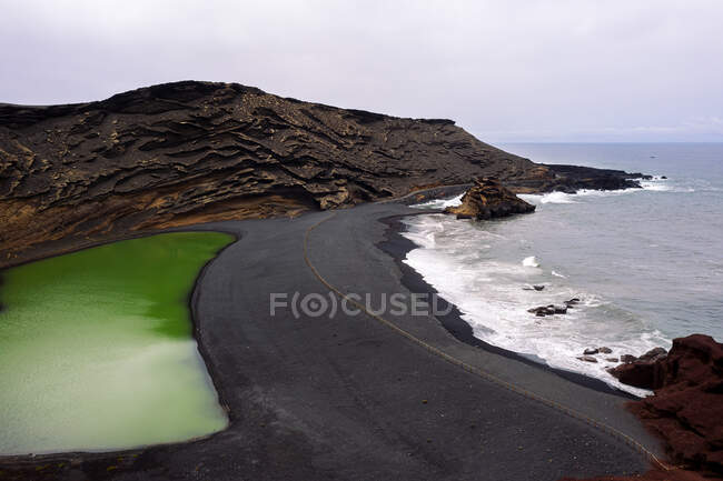 Vista aérea del Charco Verde contra el océano espumoso en las tierras altas de Golfo Yaiza Lanzarote Islas Canarias España - foto de stock