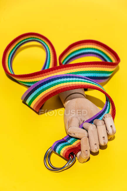 Artificial hand with long rainbow colored strap with metal buckle rings placed on yellow background in light creative modern studio — Stock Photo