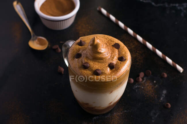 Du dessus du verre de café doux Dalgona avec garniture mousseuse servie sur la table avec rouleau de gaufrettes au chocolat et poudre de cacao — Photo de stock