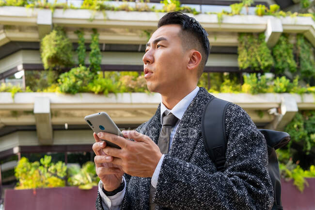 Знизу молодий етнічний чоловік-підприємець з краваткою, дивлячись подалі, розмовляючи на мобільний телефон у місті — стокове фото