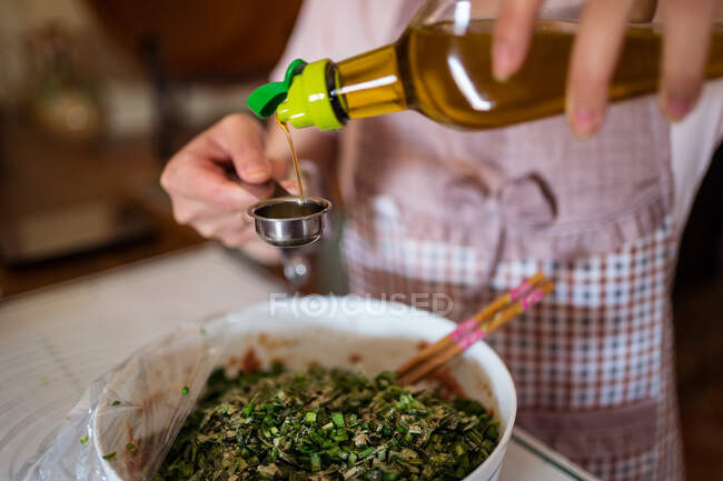 From above of crop unrecognizable housewife in apron pouring olive oil into bowl with raw minced meat and herbs while preparing stuffing for jiaozi dumplings — Stock Photo
