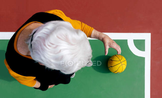 Вид зверху анонімної зрілої жінки з сірим волоссям, що стоїть на спортивному майданчику з м'ячем під час гри в баскетбол — стокове фото