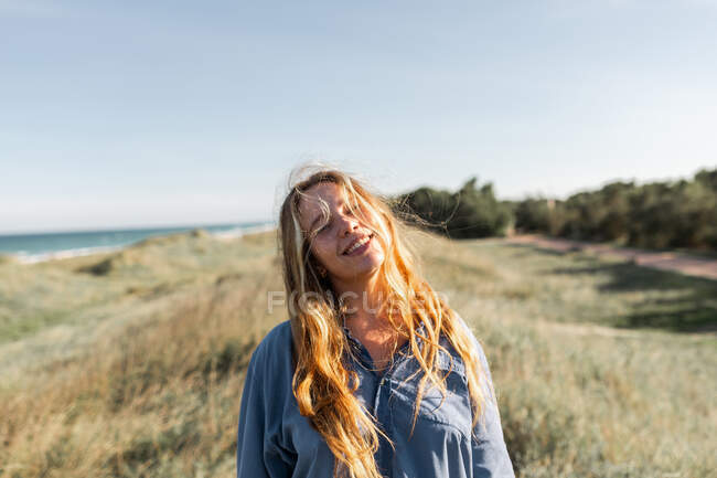 Cheerful young female in casual outfit standing on grassy meadow in summer with eyes closed — Stock Photo