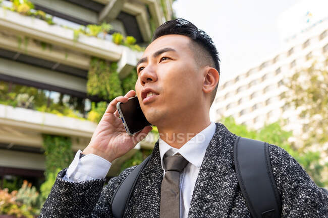 Young ethnic male entrepreneur with tie looking forward while speaking on cellphone in town — Stock Photo