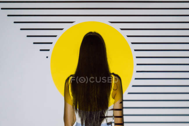 Вид ззаду на невпізнавану жінку з довгим волоссям у жовтому проекторі світло зі смугами — стокове фото