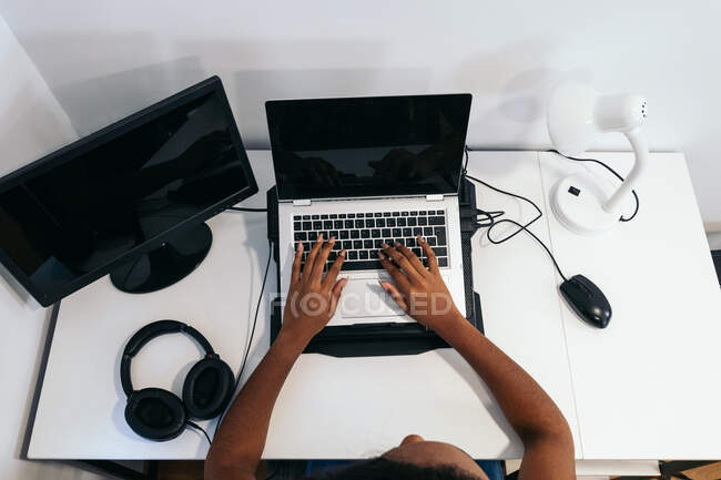 D'en haut recadrée femme afro-américaine méconnaissable assis à la table et tapant sur ordinateur portable dans la salle de lumière — Photo de stock