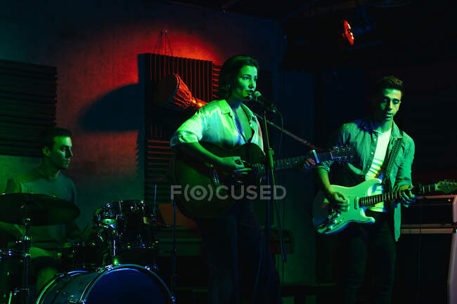 Hombre tocando la guitarra mientras mujer cantando y cantando canción en el club con luces de neón - foto de stock