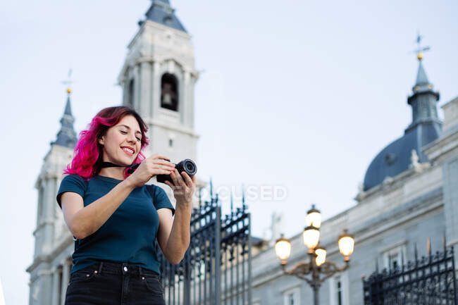 Орієнтована жінка мандрівник фотографує фотоапарат, стоячи на вулиці з вуличним ліхтарем біля старовинної будівлі з парканом у місті — стокове фото