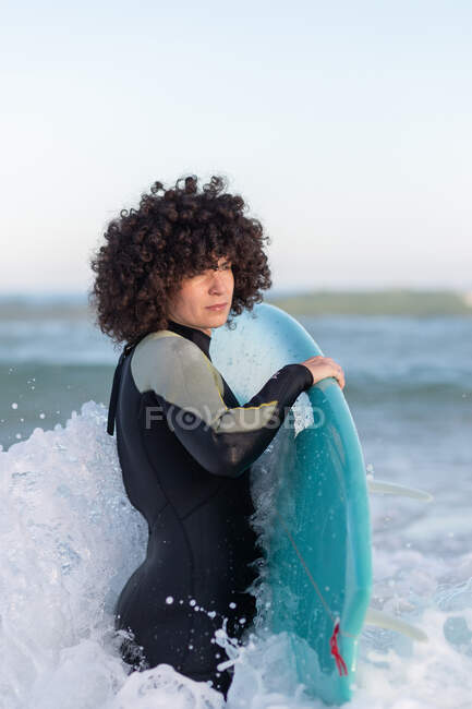 Vista lateral do jovem surfista em wetsuit na água do mar acenando com bordo desfrutando de dia de verão — Fotografia de Stock