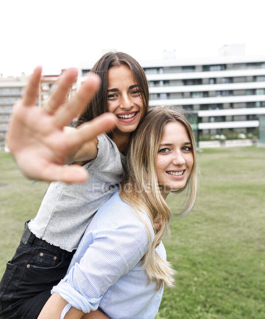 Cheerful female friends smiling and looking at camera while having fun on green grass in yard — Stock Photo