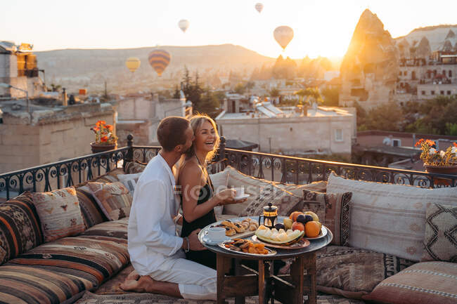 Side view of loving male kissing wife while eating dessert and drinking tea together on terrace — Stock Photo