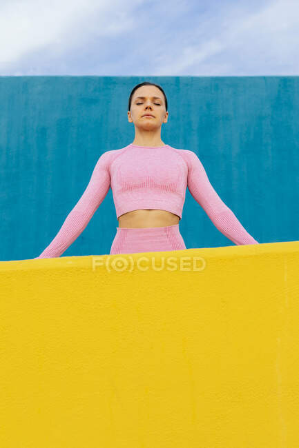 Serious concentrated female with dark hair wearing light pink activewear l against blue wall — Stock Photo