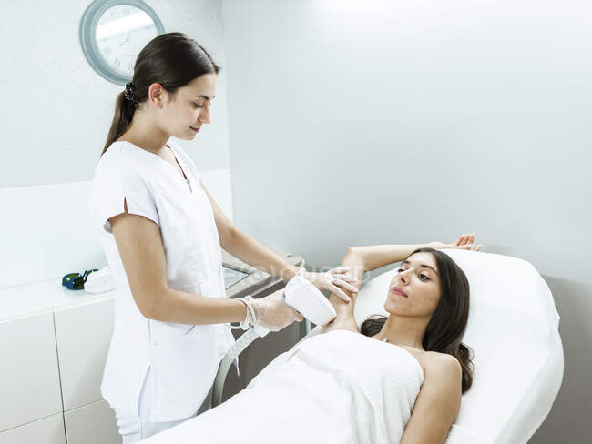 Young master doing laser hair removal procedure with professional equipment in hand in light salon — Stock Photo