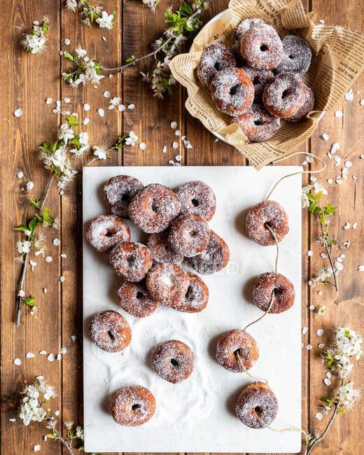 Vista superior de los apetitosos donuts prestados dispuestos en tablero blanco en mesa de madera con flores - foto de stock