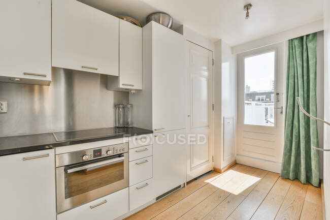 Interior de cozinha moderna com geladeira e fogão com forno elétrico embutido sob armário em casa no dia ensolarado — Fotografia de Stock