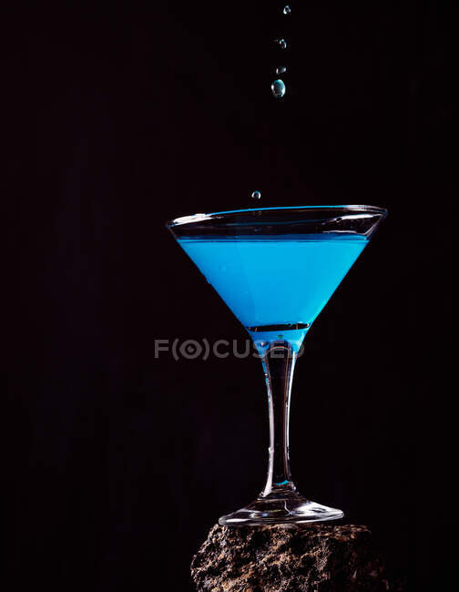 Tropfen blauer Lagunen-Cocktail in Kristallglas auf rauer Oberfläche vor schwarzem Hintergrund — Stockfoto
