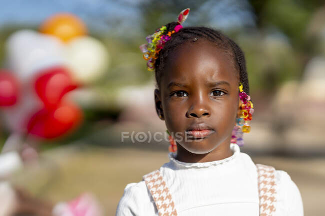 African American girl with hairstyle in stylish outfit standing and looking at camera against blurred background on street in sunny day — Stock Photo