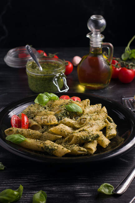 De cima de prato com deliciosa massa com molho pesto verde e tomates servidos em mesa de madeira preta — Fotografia de Stock