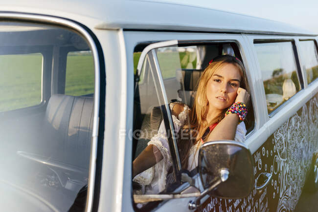 Симпатичная блондинка сидит в винтажном фургоне и прислоняется к окну в солнечный день. — стоковое фото