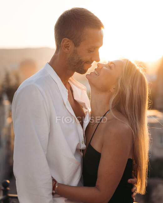 Vista laterale di abbracciare l'uomo e la donna innamorati in piedi insieme sulla strada e guardarsi l'un l'altro contro il tramonto — Foto stock