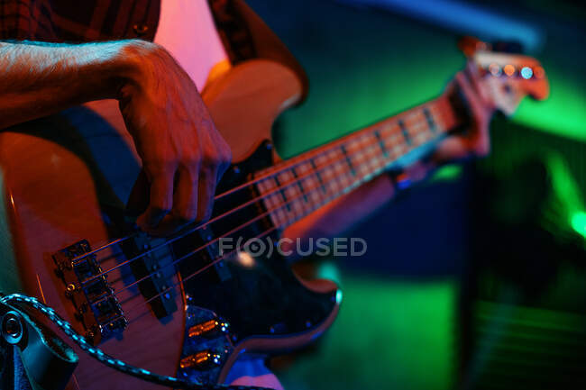 Crop anonimo chitarrista maschile suonare la chitarra elettrica nel club con luci verdi al neon — Foto stock