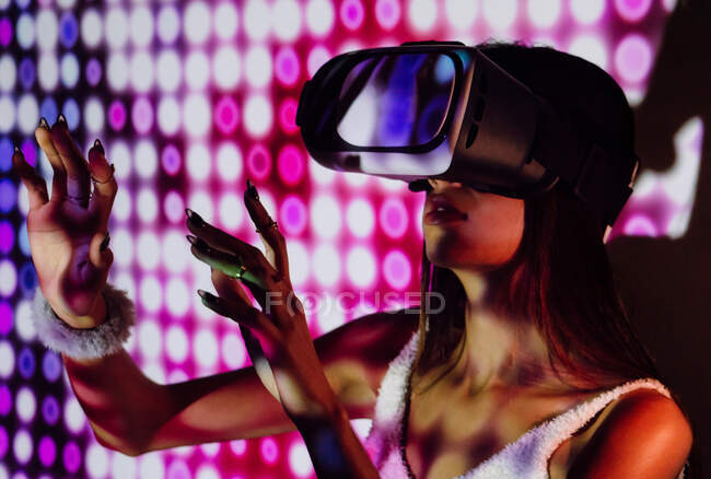 Fêmea focada com tons no corpo experimentando a realidade virtual no fone de ouvido moderno em luzes do projetor — Fotografia de Stock