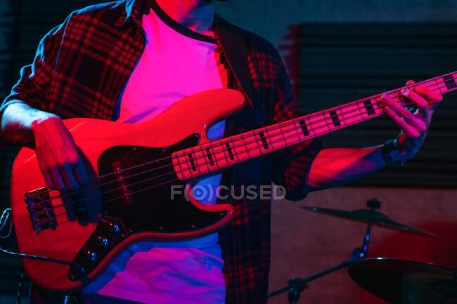 Crop anonymous male guitarist playing electric guitar in club with neon purple and blue lights — Stock Photo