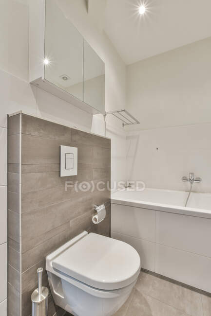 Toilet mounted on tiled wall under cupboard near bathtub in light modern restroom — Stock Photo