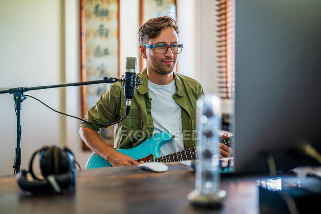 Male musician playing electric guitar near microphone in recording studio — Stock Photo