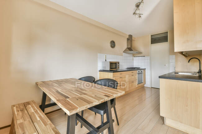 Interior da cozinha moderna com paredes bege móveis de madeira armários fogão micro-ondas forno faixa capuz mesa de jantar e cadeiras — Fotografia de Stock