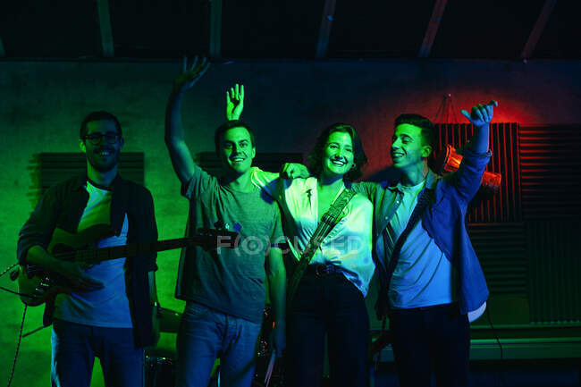 Band group saying goodbye to the public after concert with guitars and drums while woman singing and performing song in club with neon lights — Stock Photo