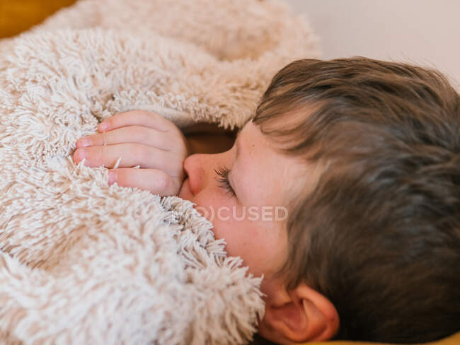 Бічний погляд на хворого хлопця, який страждає від грипу, лежить з закритими очима під ковдрою на дивані і спить вдома. — стокове фото