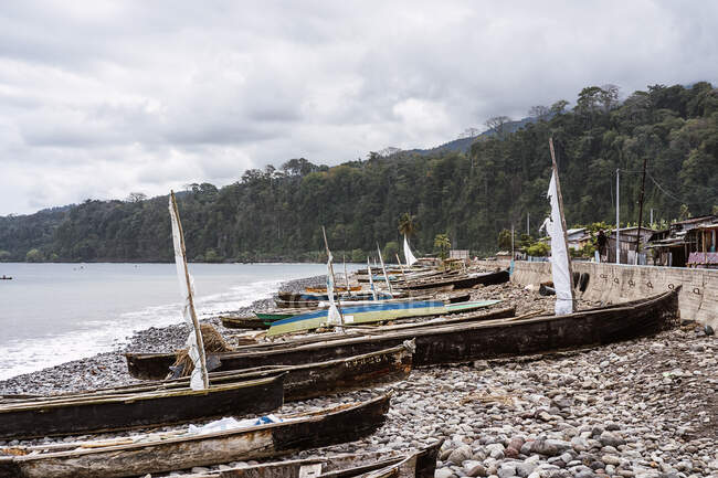 Vieux bateaux en bois amarrés sur la côte rocheuse près de l'océan calme contre les arbres verts à So Tom et Prncipe sous un ciel nuageux en plein jour — Photo de stock
