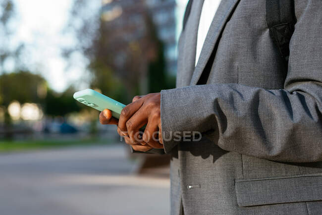 Crop side view African American businessman in formal wear with backpack browsing mobile phone in downtown — Stock Photo