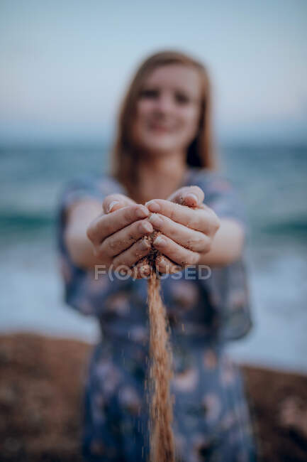 Неузнаваемая женщина в платье с горсткой песка, стоящего на пляже возле моря в летний день — стоковое фото
