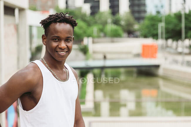 Positiver afroamerikanischer Mann lächelt strahlend, während er auf Brücke steht und in die Kamera schaut — Stockfoto