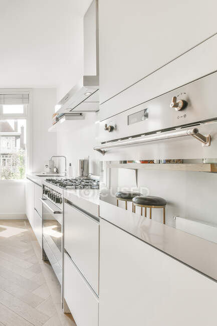 Інтер'єр просторої кухні з мінімалістичними білими меблями і сучасною технікою в світлій квартирі — стокове фото