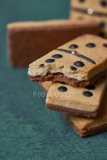 Heap of sweet tasty crunchy dominoes shaped cookies with black dots and bitten piece scattered on green surface in light room — Stock Photo