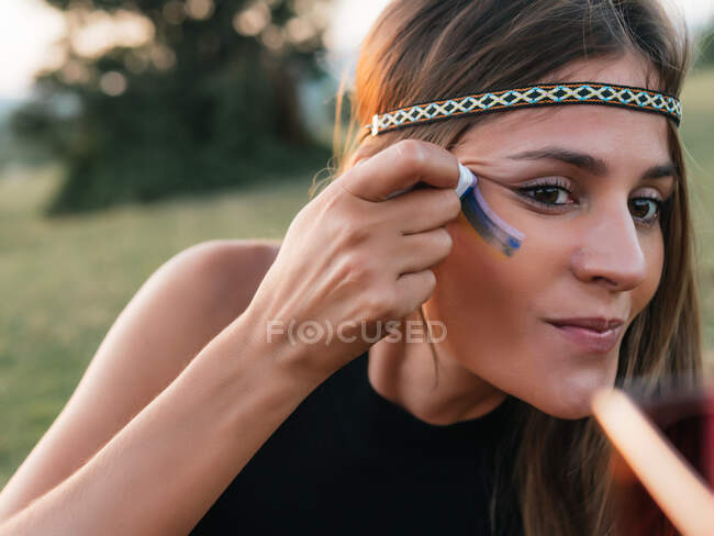 Close-up de uma mulher pintando um arco-íris na bochecha com um pau — Fotografia de Stock