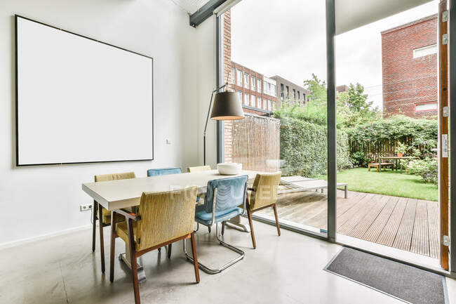 Chairs at desk with lamp placed in light room with whiteboard and glass door overlooking patio with grassy lawn and plants — Stock Photo