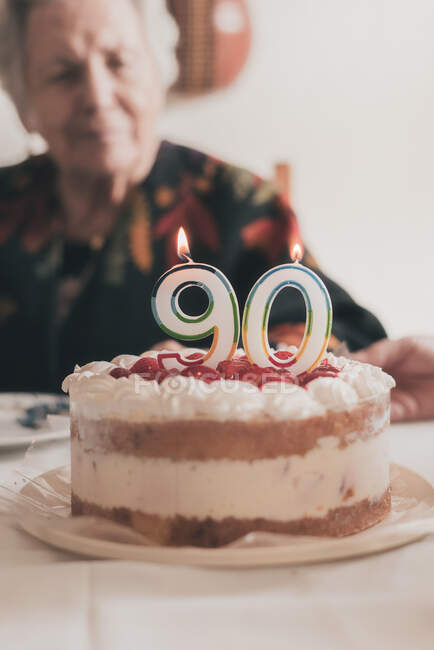 Femme âgée soufflant des bougies sur le gâteau d'anniversaire puis applaudissant les mains tout en célébrant le 90e anniversaire avec un parent à la maison — Photo de stock
