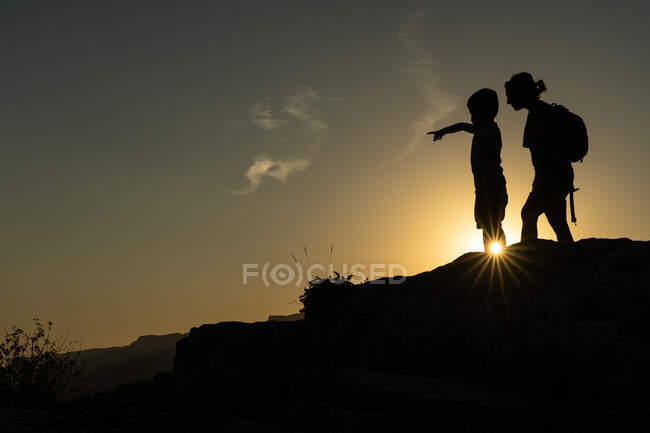 Silueta de las piernas de una mujer haciendo trekking en la montaña con el sol creando una estrella del sol con su pie al atardecer - foto de stock