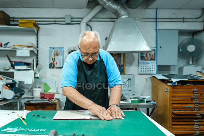 Crop unrecognizable male artisan in casual clothes and apron folding cover of album while standing at workbench in traditional printing studio — Stock Photo