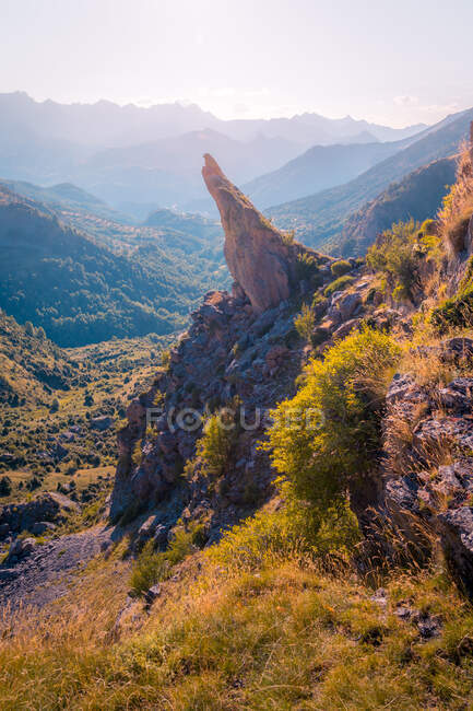 Rough stony cliff located near green hilly area covered with plants against cloudless sky on sunny summer day in Spain — Stock Photo